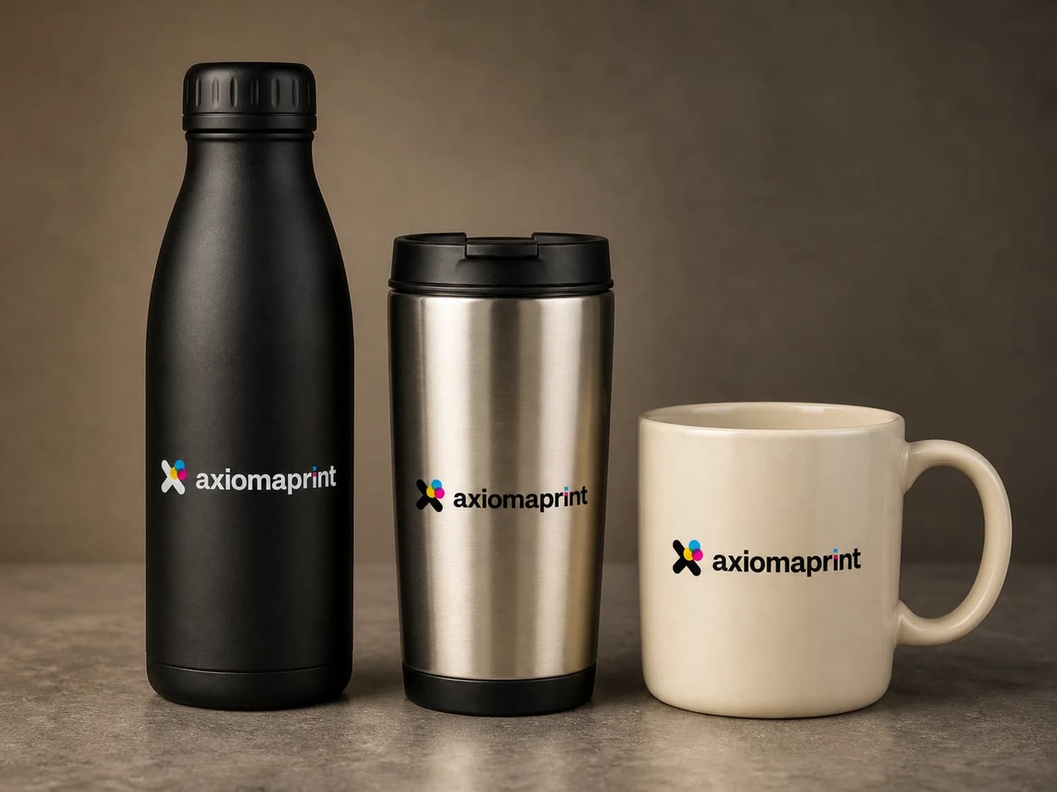 Botella térmica negra, vaso de acero con tapa y taza de cerámica color crudo alineados sobre una encimera de piedra