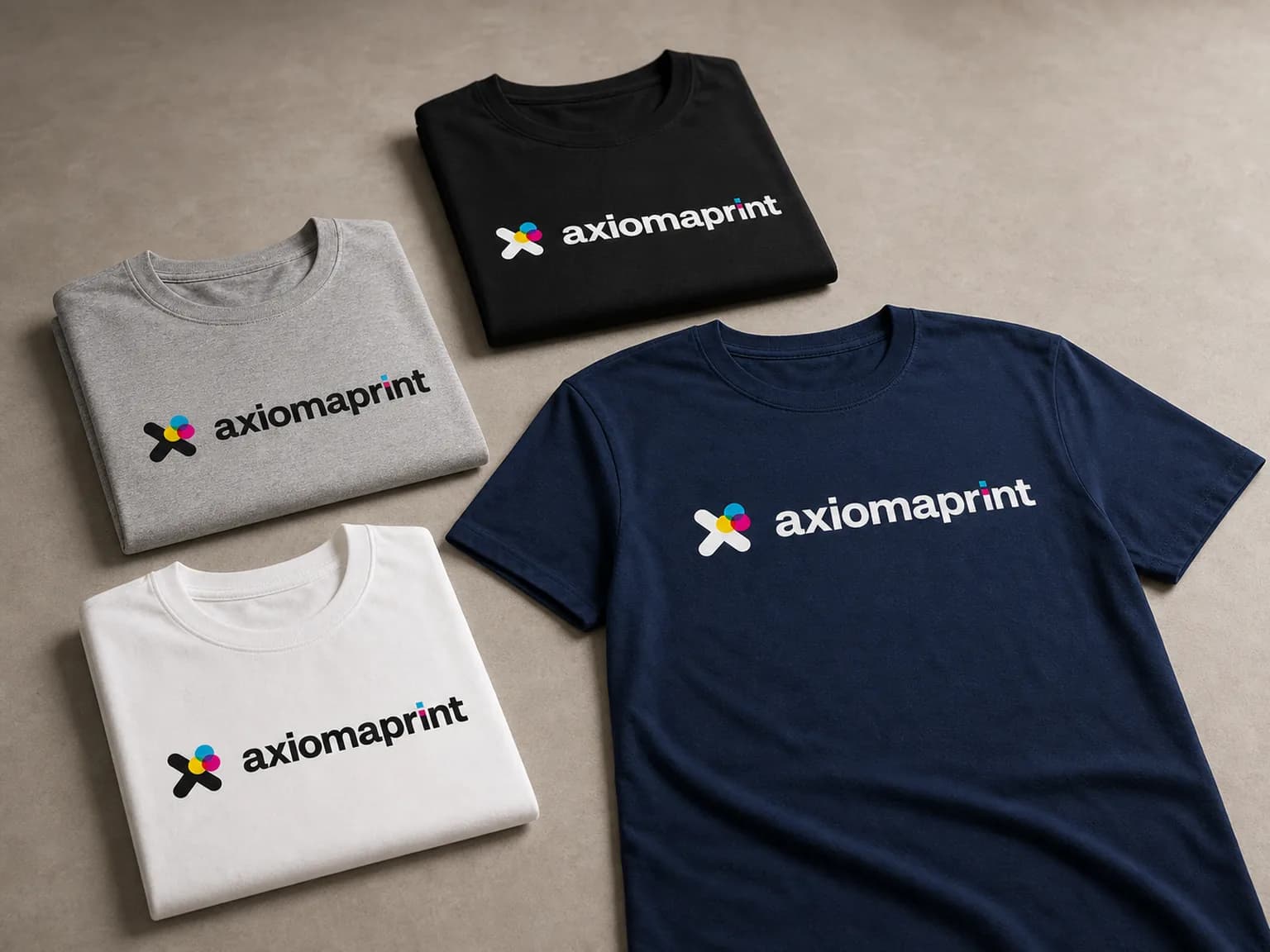 Cuatro camisetas en negro, gris, blanco y azul marino, tres dobladas y una extendida, con el logotipo en el pecho