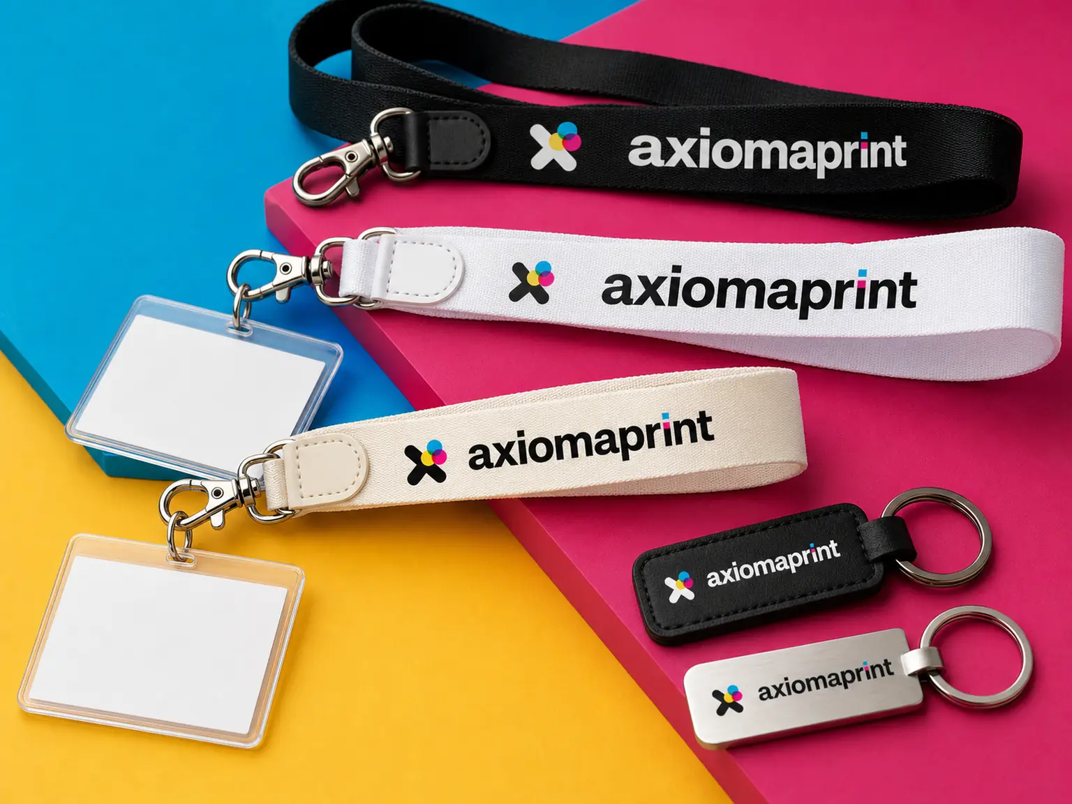 Tres lanyards negro, blanco y crudo con mosquetón y portatarjetas, junto a dos llaveros rectangulares sobre fondos de colores